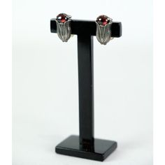 a pair of earrings with red stones are on a black display stand against a white background