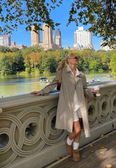 a woman standing on a bridge next to a river with trees and buildings in the background