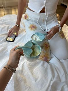 two women are sitting on a bed and one is holding a bowl with food in it