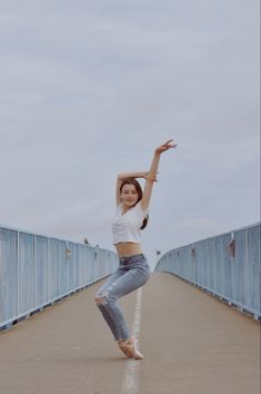 a woman is dancing on a bridge with her arms in the air while wearing jeans