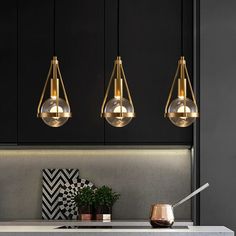 three pendant lights hanging from the ceiling above a kitchen counter with a potted plant