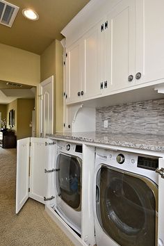 a washer and dryer are in the middle of a room with white cabinets