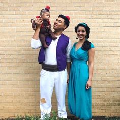 a man and woman are standing in front of a brick wall with a baby on his shoulders