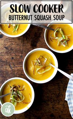 four bowls filled with soup sitting on top of a wooden table next to a spoon