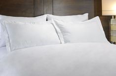 a bed with white sheets and pillows in a hotel room at the foot of a night stand