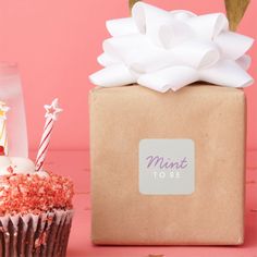 a cupcake next to a box with a candle on it and a pink background