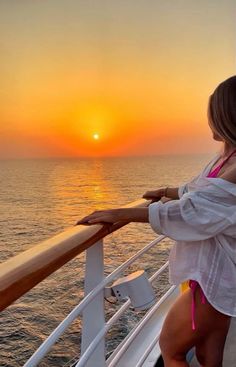 a woman standing on the deck of a boat watching the sun set over the ocean