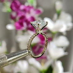 a close up of a diamond ring with flowers in the background