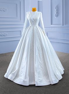 a white wedding dress with long sleeves and a train on display in front of a blue wall