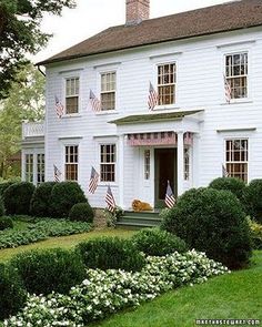 a large white house with american flags on the windows and bushes in front of it