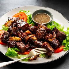 a white plate topped with meat and veggies next to a bowl of dipping sauce