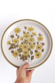 a hand holding a plate with yellow flowers on it