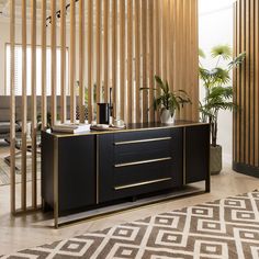 a living room with a black and gold sideboard next to a plant in a vase