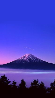 a mountain covered in snow at dusk with trees around it and the sky filled with clouds