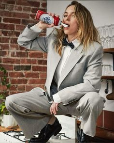 a woman in a suit drinking from a can