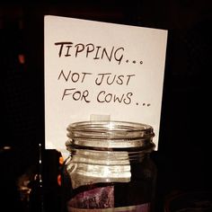 a jar filled with lots of stuff sitting on top of a table next to a sign that says tipping not just for cows