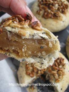 a person is holding some kind of doughnut with pecans on top and other pastries in the background