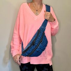 a woman in pink shirt holding up a blue fanny bag with zippers on it