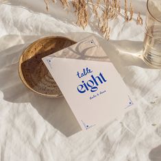 a table sign sitting on top of a white blanket next to two glasses and a bowl