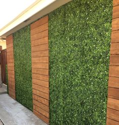 a wooden wall covered in green plants next to a sidewalk