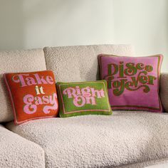 three pillows sitting on top of a white couch next to each other in different colors