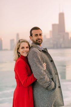 a man and woman standing next to each other in front of the ocean with city skyline behind them