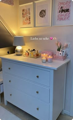 a white dresser with candles and pictures on the wall