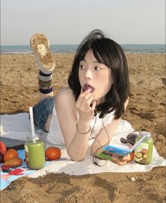 a woman laying on top of a sandy beach next to fruit and juices in front of her