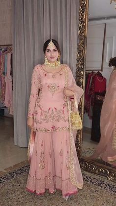 a woman standing in front of a mirror wearing a pink outfit with gold details on it