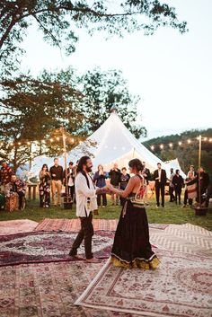 a man and woman dancing in front of a crowd at an outdoor event with string lights