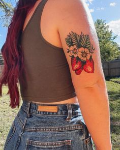 a woman with a strawberry tattoo on her left arm and shoulder, standing in the grass