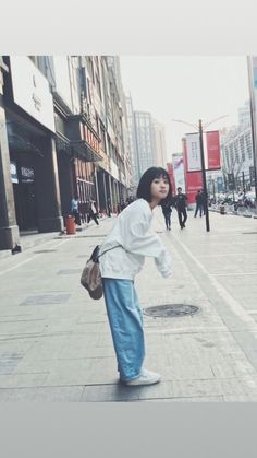 a woman is standing on the sidewalk with her hand in her pocket and looking down