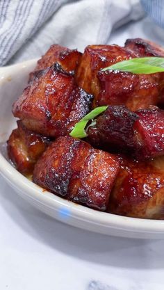 a white bowl filled with cooked meat and garnished with green onion sprigs