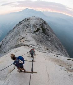 three people climbing up the side of a mountain with their backpacks on and holding onto some metal bars