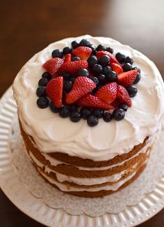 a cake with white frosting and fresh berries on top is sitting on a plate