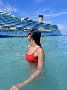 a woman in a red swimsuit is floating in the ocean next to a cruise ship