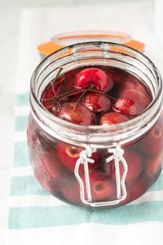 a glass jar filled with cherries sitting on top of a blue and white table cloth