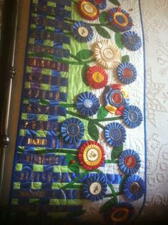 a close up of a quilt on a bed with flowers and ribbons attached to it