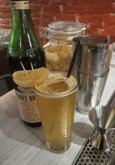 a bottle of beer next to a glass filled with ice and orange slices on a table