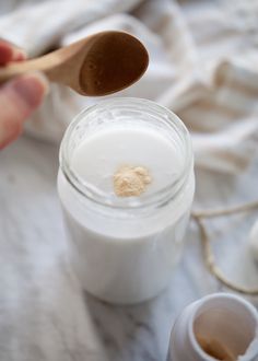 a person holding a wooden spoon over a jar of yogurt next to two cups