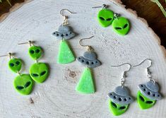 green alien earrings and earring set sitting on top of a piece of tree trunk