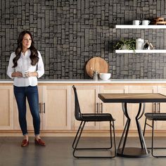 a woman standing in front of a kitchen counter with two chairs and a wooden table