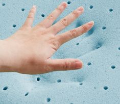 a person's hand on top of a blue mattress with holes in the foam