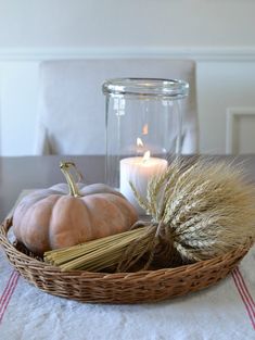 a basket filled with pumpkins and wheat on top of a table next to a candle