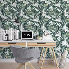 a desk with a laptop on top of it next to a wallpaper that has palm leaves