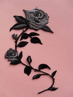 an embroidered rose on a pink background with black leaves and stems in the shape of flowers