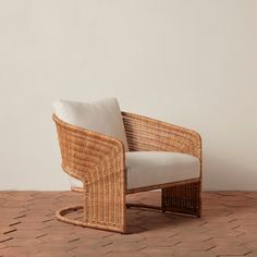 a wicker chair sitting on top of a brick floor next to a white wall