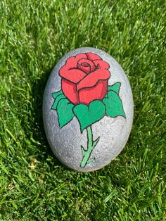 a rock with a rose painted on it sitting in the middle of some green grass