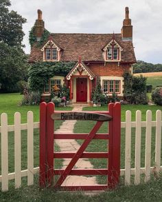 a red gate is in front of a house with a white picket fence and green grass