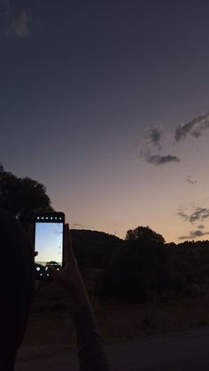 a person holding up a cell phone to take a photo with the sun setting in the background